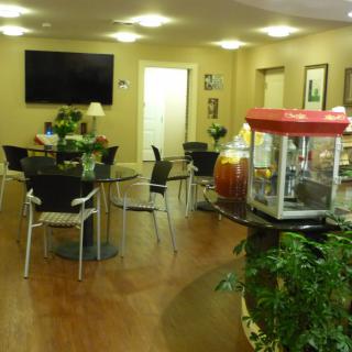 A cozy lobby area featuring tables and chairs, a popcorn machine, television, and decorative plants.