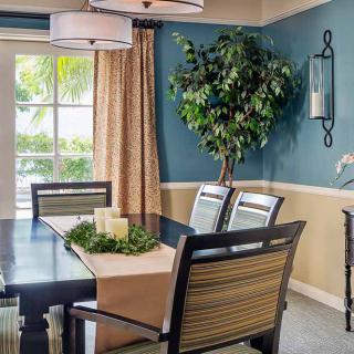 A cozy dining room with a table set for four, featuring a green plant and natural light from a large window.