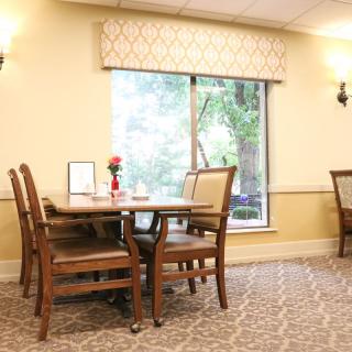 A cozy dining area with a table set near a large window, surrounded by cushioned chairs in a warmly lit room.