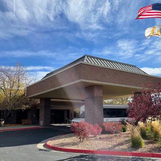 A modern building entrance with a flag and landscaped surroundings under a blue sky.