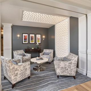 A modern lobby seating area featuring patterned chairs, a round table, and wall artwork.