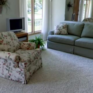 A cozy living room featuring a sofa, armchair, television, and large windows letting in natural light.