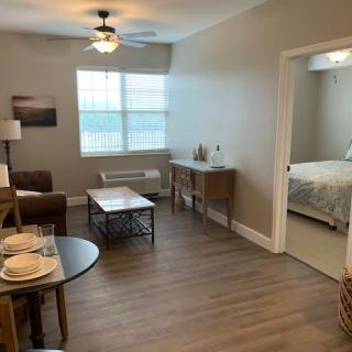 A modern apartment interior with a living room, dining area, and visible bedroom.