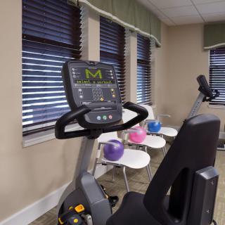 A fitness room with an exercise bike and fitness balls on tables.