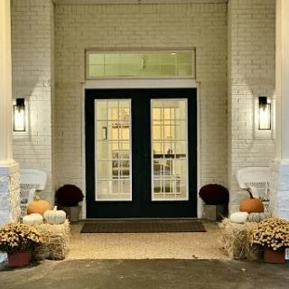 A warmly lit front entrance decorated for autumn with pumpkins and flowers.