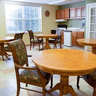 An empty dining area with wooden tables and chairs, adjacent to a small kitchen.