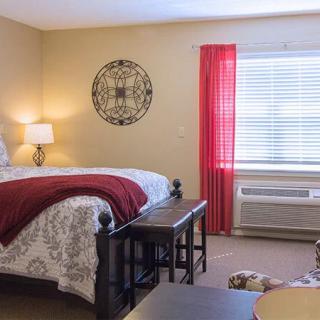 A cozy bedroom with a neatly made bed, decorative wall art, and a window with red curtains.