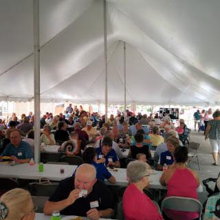 A lively gathering under a tent with people enjoying food and conversation.