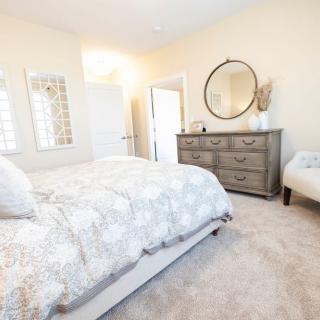A cozy bedroom with a bed, dresser, and mirror, decorated in neutral tones.