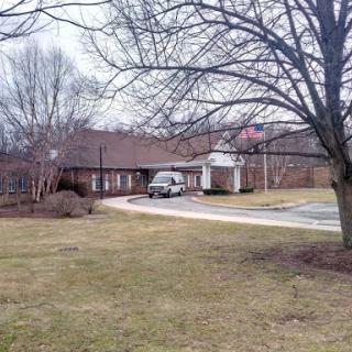 A serene view of a building surrounded by trees and grass, with a vehicle parked nearby.