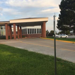 A view of a building entrance with a clear sky backdrop, surrounded by grass and trees.