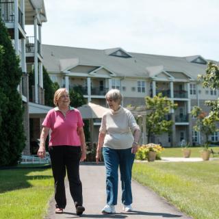 Two elderly people taking a walk outside a retirement community building.