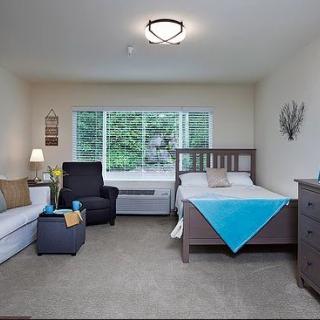 A cozy bedroom with a bed, armchair, sofa, and dresser, featuring a large window.