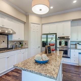 A modern kitchen featuring a central island with a granite countertop, white cabinetry, and stainless steel appliances.