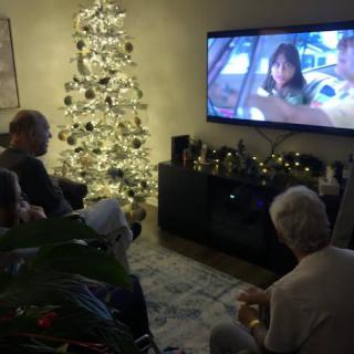A family gathers around the TV in a decorated living room during Christmas.