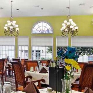 A well-lit dining room with chandeliers, elegantly set tables, and large windows.