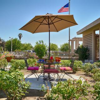 A sunny garden patio with outdoor seating, an umbrella, and a view of the American flag.