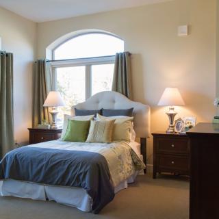 A cozy bedroom featuring a neatly made bed with multiple pillows, flanked by two bedside tables and lamps, with curtains framing a large window.