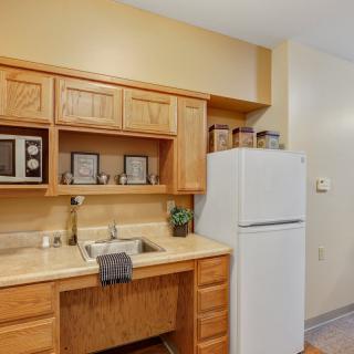 A compact kitchen area featuring wooden cabinets, a white refrigerator, microwave, and a sink with a beige countertop.