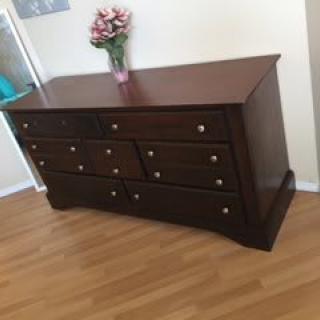 A wooden dresser with multiple drawers, topped with a flower vase, on a hardwood floor.