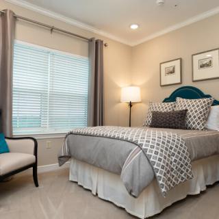 A well-decorated bedroom featuring a neatly made bed, a cozy chair, and soft lighting.