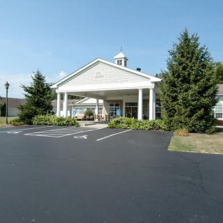 A white building with a columned entrance set against a clear blue sky, surrounded by trees and adjacent to a parking lot.
