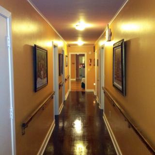 A well-lit hallway with paintings on the walls and a polished wooden floor.