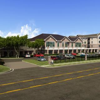 A large residential building with a parking lot and surrounding trees lining the street.