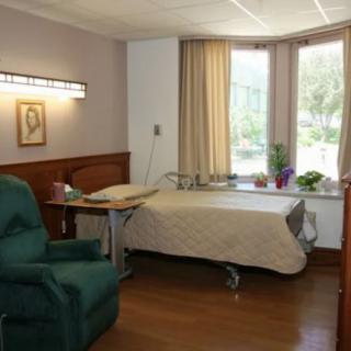 A hospital patient room with a bed and a comfortable chair by the window.