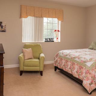 A cozy bedroom with a neatly made bed and an armchair by the window.