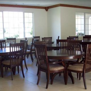 An empty dining area with multiple wooden tables and chairs arranged near large windows.