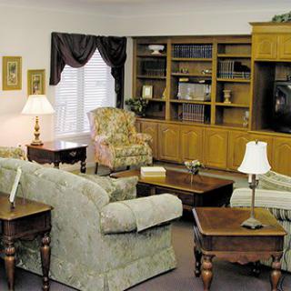 A cozy living room with sofas, an armchair, wooden tables, and a large bookshelf.