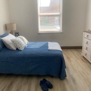 A minimalist bedroom with blue bedding and a dresser by the window.