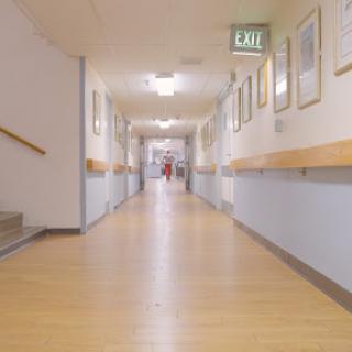 A quiet hallway in a hospital, featuring wooden flooring and framed artworks on the walls.