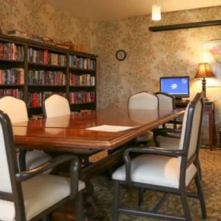 A cozy conference room with a wooden meeting table, surrounded by bookshelves and equipped with a computer.