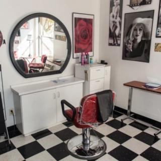 A stylish hair salon with a retro red chair, large round mirror, and checkerboard flooring.