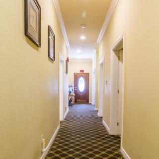 A well-lit hallway with carpeted flooring and framed pictures on the walls.