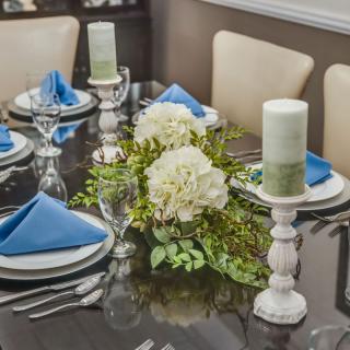 An elegantly set dining table with blue napkins, white candles, and a floral centerpiece.