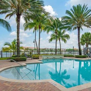 A tranquil outdoor swimming pool surrounded by palm trees with a view of the waterfront.