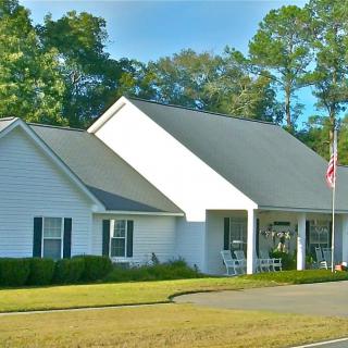 A suburban house with a neatly maintained lawn and an American flag on the porch, set against a backdrop of trees.