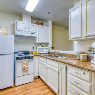 A cozy kitchen with white cabinets, a refrigerator, stove, and various countertop appliances.
