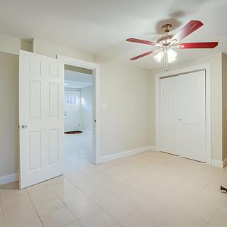 An empty bedroom with a ceiling fan, tile flooring, a closed closet, and an open doorway.