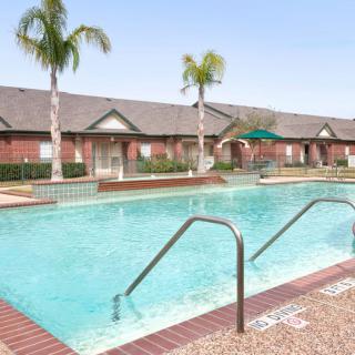 An outdoor swimming pool in a residential area, surrounded by palm trees and brick buildings.
