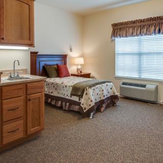A cozy bedroom with a single bed, wooden cabinetry, and a window with blinds.