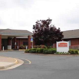 A brick hospital building with an entrance and a clearly visible sign near the driveway.