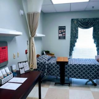A well-arranged hospital room featuring a bed, small table, and window with curtains.