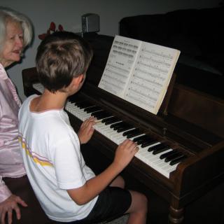 A child receives a piano lesson from an elderly person.