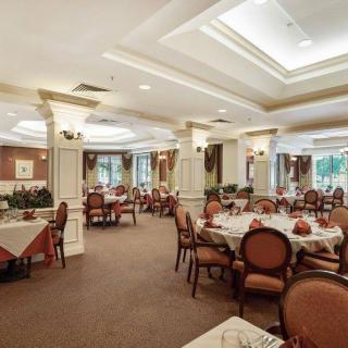 An elegant dining room with neatly arranged tables and chairs, featuring tasteful decorations and ample natural lighting through large windows.