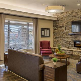 A cozy living room with modern decor, featuring a stone fireplace and large windows.