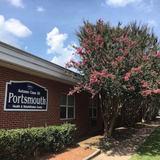 A brick building with a sign for Portsmouth, surrounded by a flowering tree and a partly cloudy sky.